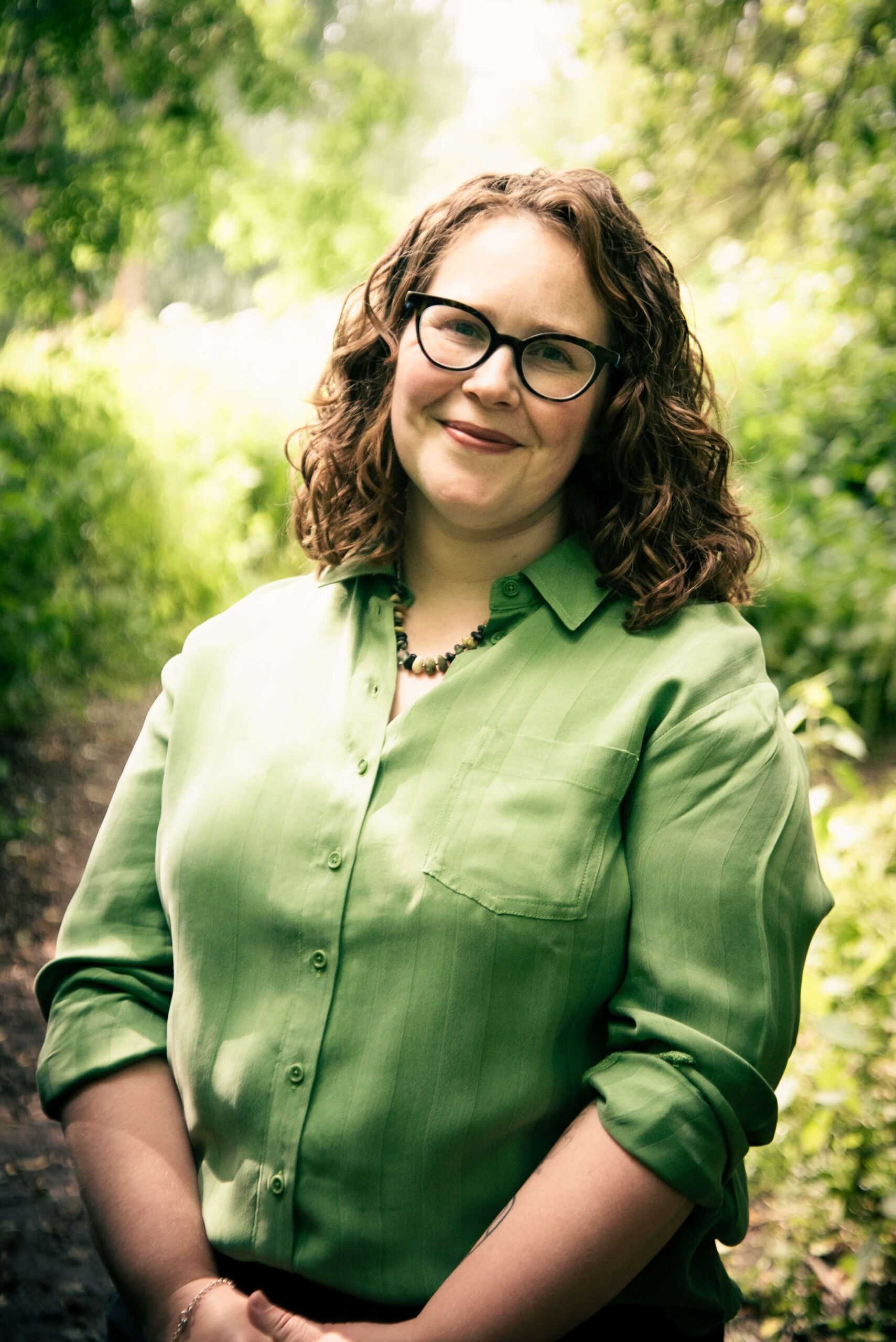 Annabell Webb is a white woman with brown curly hair and glasses. She wears a green shirt and is smiling facing the camera.